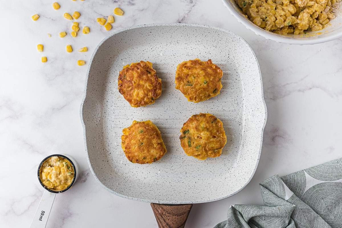 Panqueques de maíz cocidos y dorados en una sartén blanca.